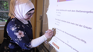 Eine Frau kreuzt die Lsung einer bung am Whiteboard an. Foto: Bildungsfilm